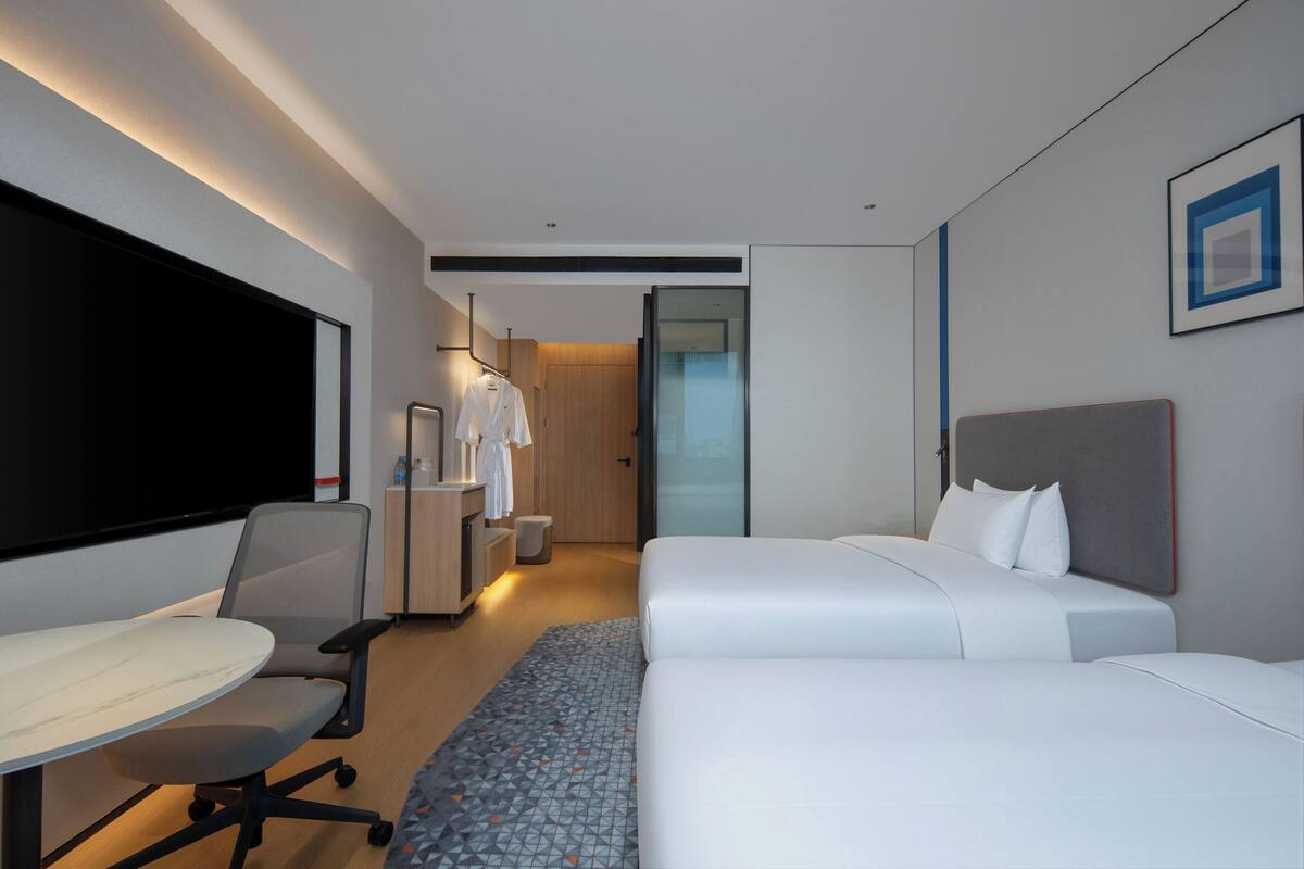 A hotel room with a bed, a desk, a chair, a TV, and a wardrobe.
