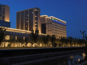 A modern hotel with multiple high-rise buildings, a river in the foreground, and a well-lit facade. - Holiday Inn Express Suzhou SIP Suliu Road by IHG (Suzhou)