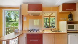 Cocina compacta con estufa a gas, lavamanos y microondas, armarios de madera y vistas a zonas verdes.