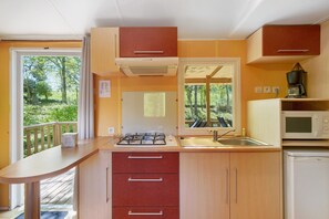 Une cuisine compacte équipée d’une cuisinière à gaz, d’un évier et d’un four à micro-ondes, avec des meubles en bois et une vue sur la verdure environnante.