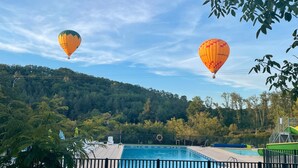 Una piscina con una valla alrededor, árboles y globos aerostáticos al fondo.