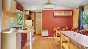 Una cocina compacta con estufa a gas, un lavamanos y una ventana. Hay un comedor con mesa y sillas, y un banco empotrado con cojín.