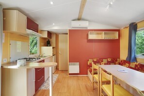 Une cuisine compacte équipée d’une cuisinière à gaz, d’un évier et d’une fenêtre. On y trouve également un coin repas avec une table et des chaises, ainsi qu’un banc intégré avec un coussin.