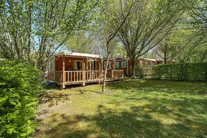Une cabane en bois dotée d’une terrasse, entourée d’arbres et d’herbe.