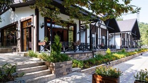 A building with a stone-paved entrance, wooden steps, and a covered outdoor seating area with tables and chairs.