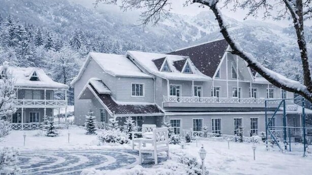 A large, multi-story building with a symmetrical facade, a covered porch, and a snow-covered landscape.