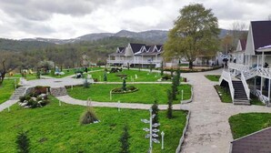 Um resort com vários edifícios tipo chalé, uma área gramada central com caminhos e montanhas ao fundo.