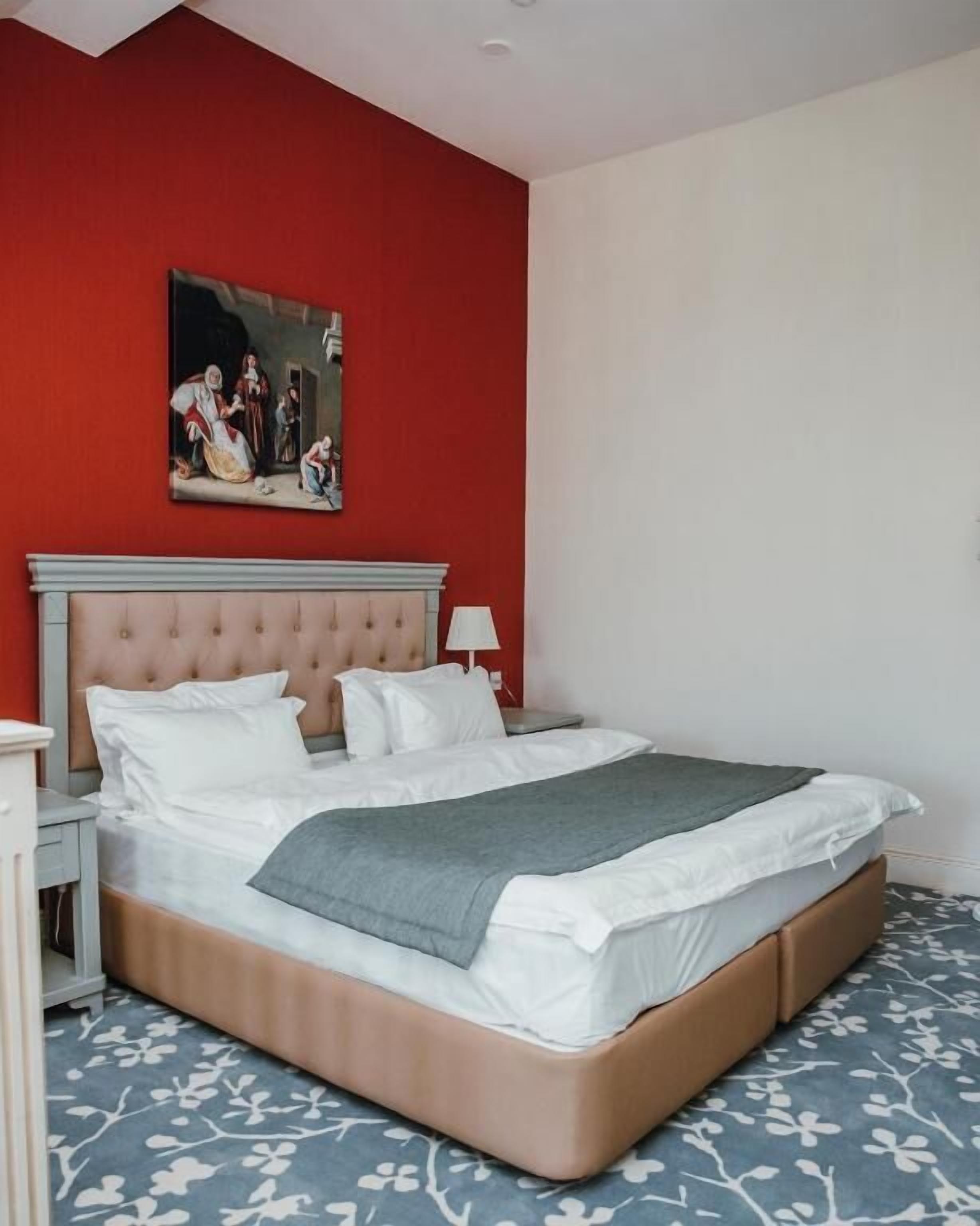 A bedroom with a large bed, a nightstand, a lamp, and a painting on the wall.