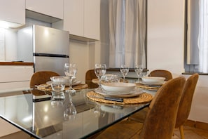 A modern kitchen with a glass dining table set for six, equipped with wine glasses and plates.