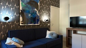 Ett modernt vardagsrum med en blå soffa, en stor abstrakt målning och en platt-TV placerad på ett träställ.