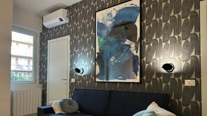 Ett modernt vardagsrum med en mörkblå soffa, abstrakt väggkonst och ett fönster med utsikt över byggnader.