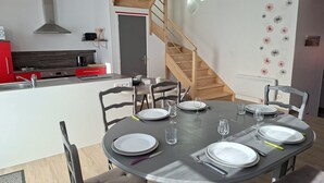 Een moderne keuken met een ingebouwde kookplaat, een houten trap en een eethoek voor vier personen, compleet met witte borden en glazen.
