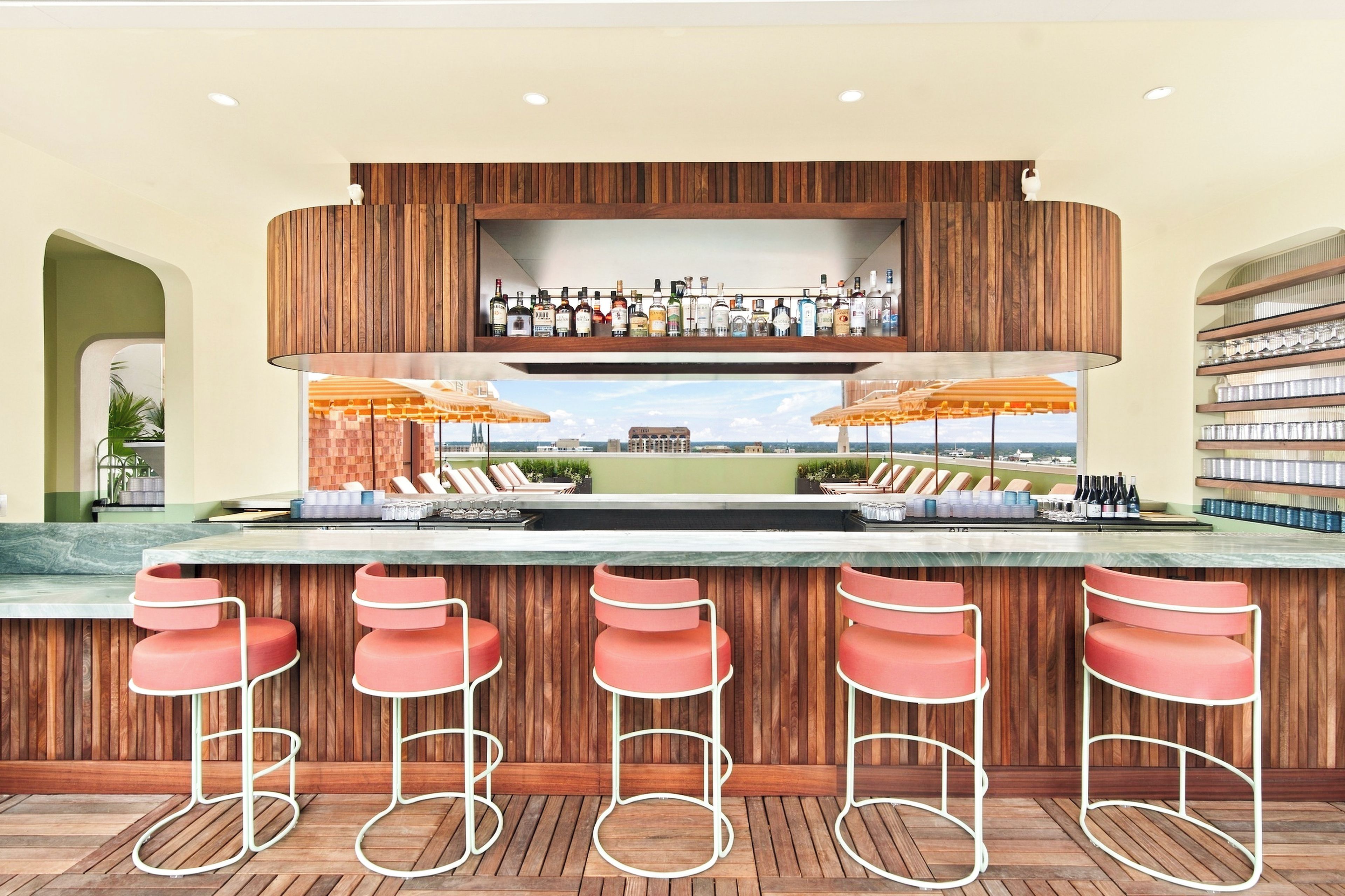 A bar area with a wooden bar counter, multiple stools, and a view of the cityscape.