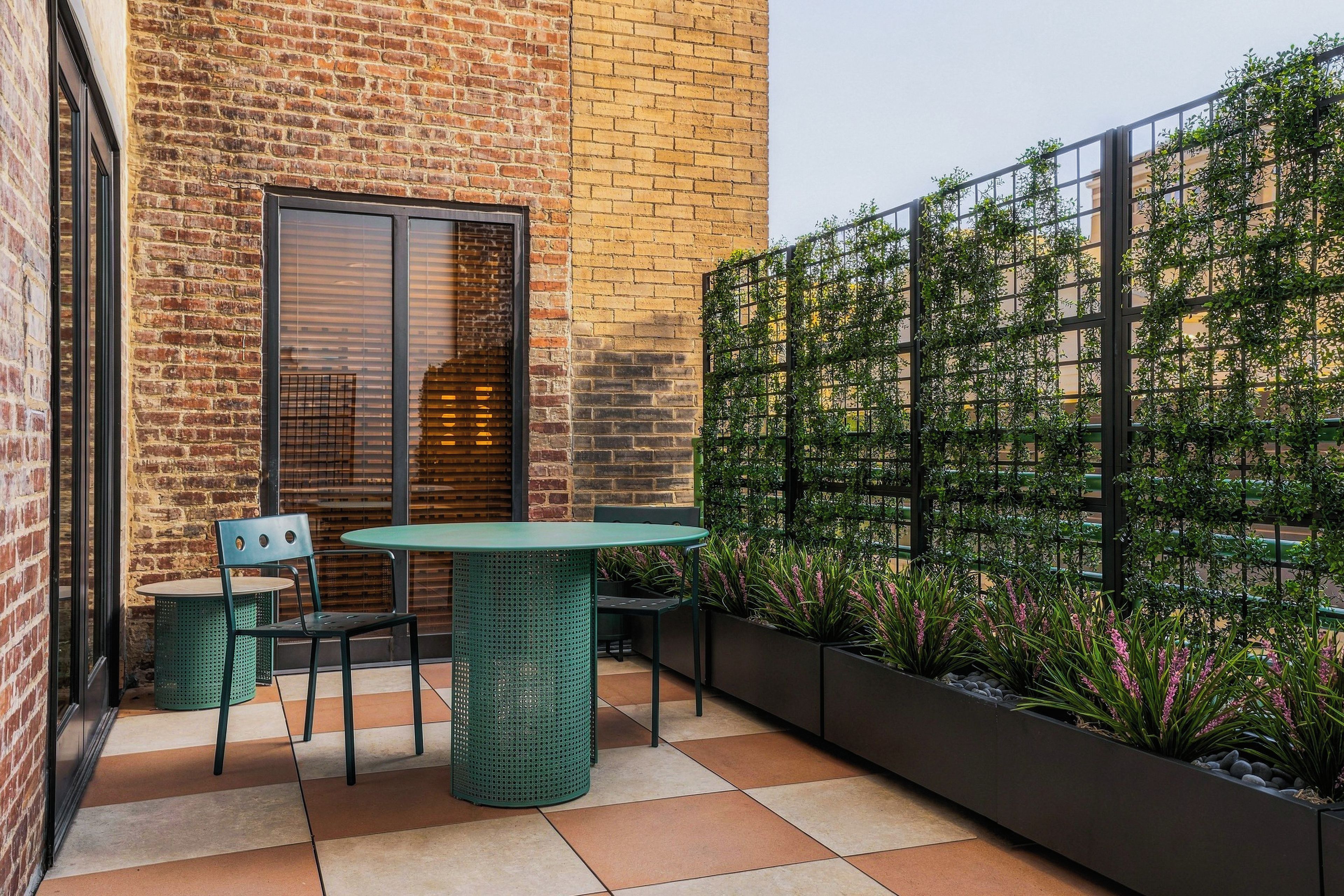 A patio with a brick wall, a glass door, a green table and chairs, and a vertical garden.