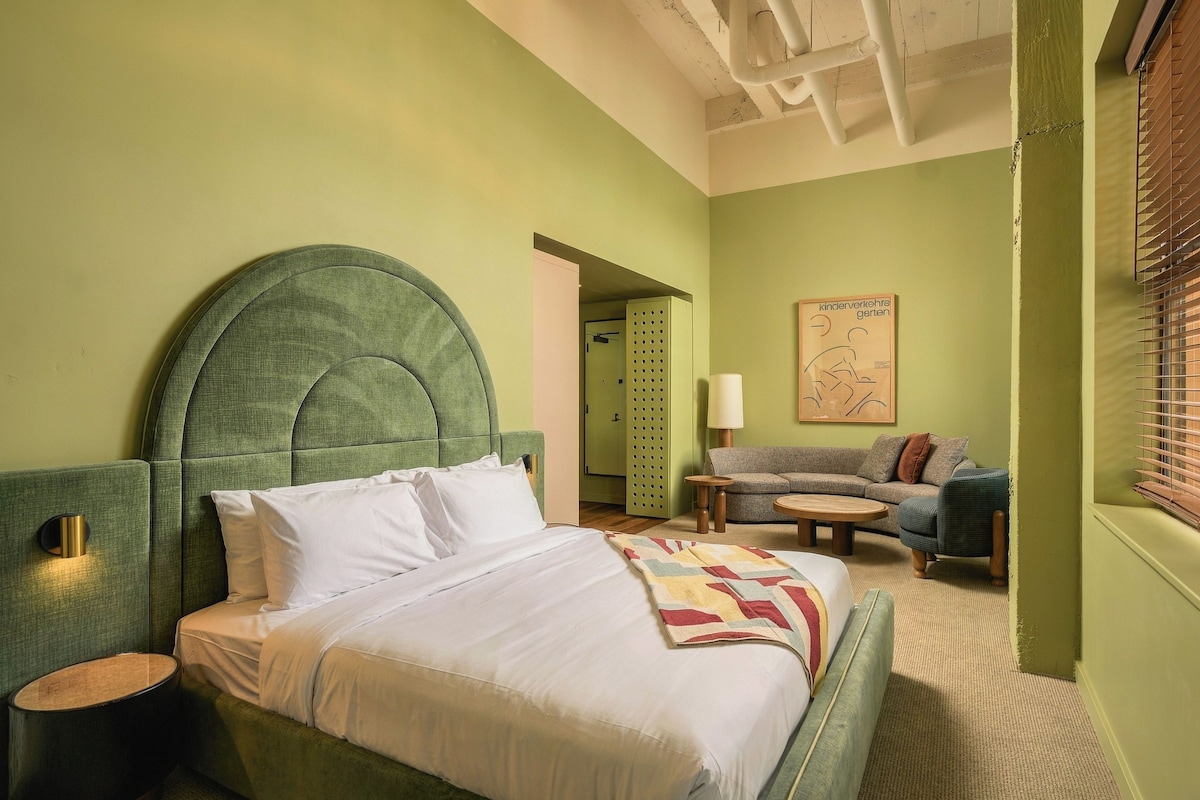 A room with a bed, a sofa, a small table, and a wall with a picture.