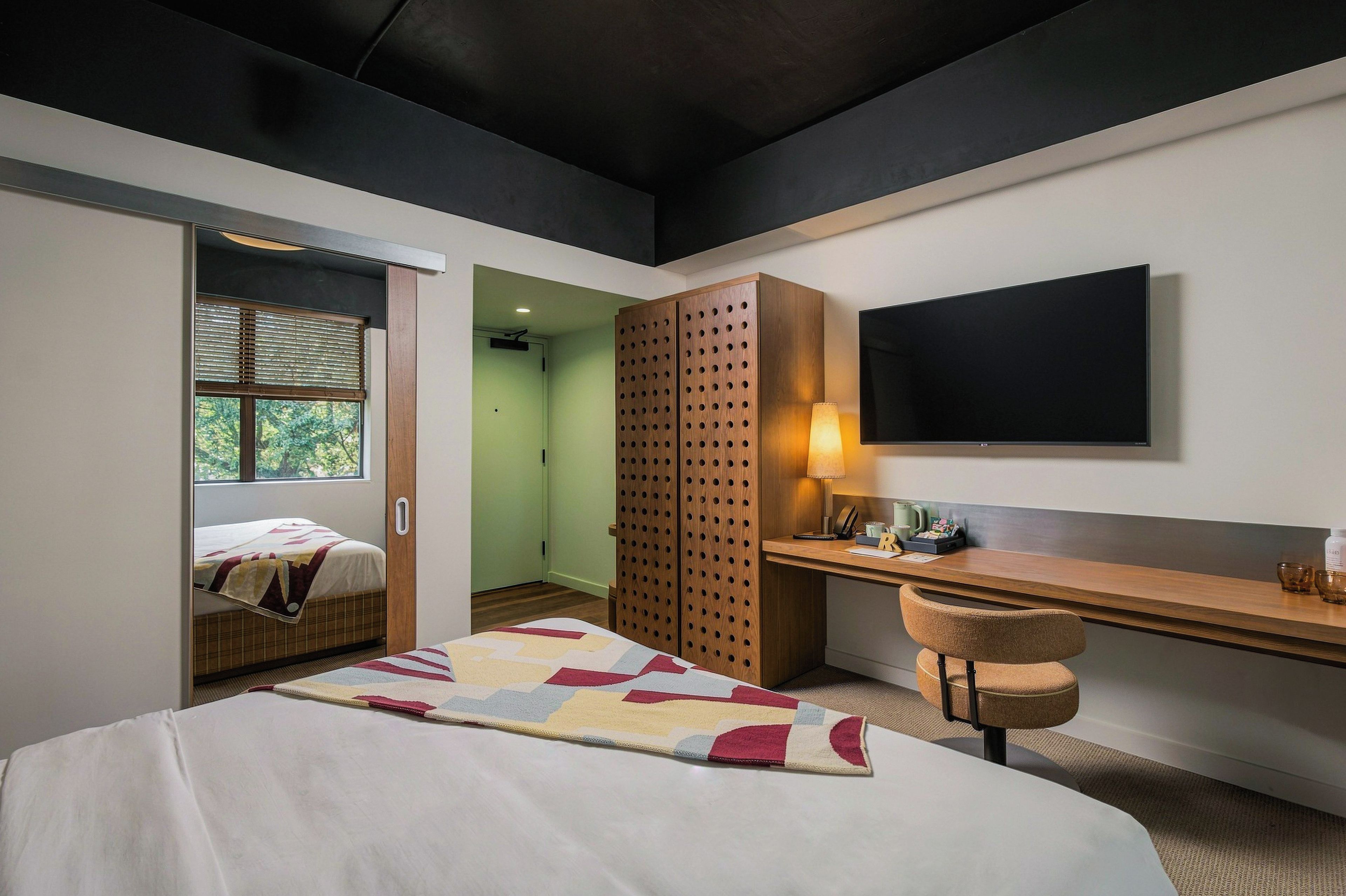 Une chambre d’hôtel moderne équipée d’un lit, d’un bureau, d’une chaise, d’une télévision et d’une armoire.