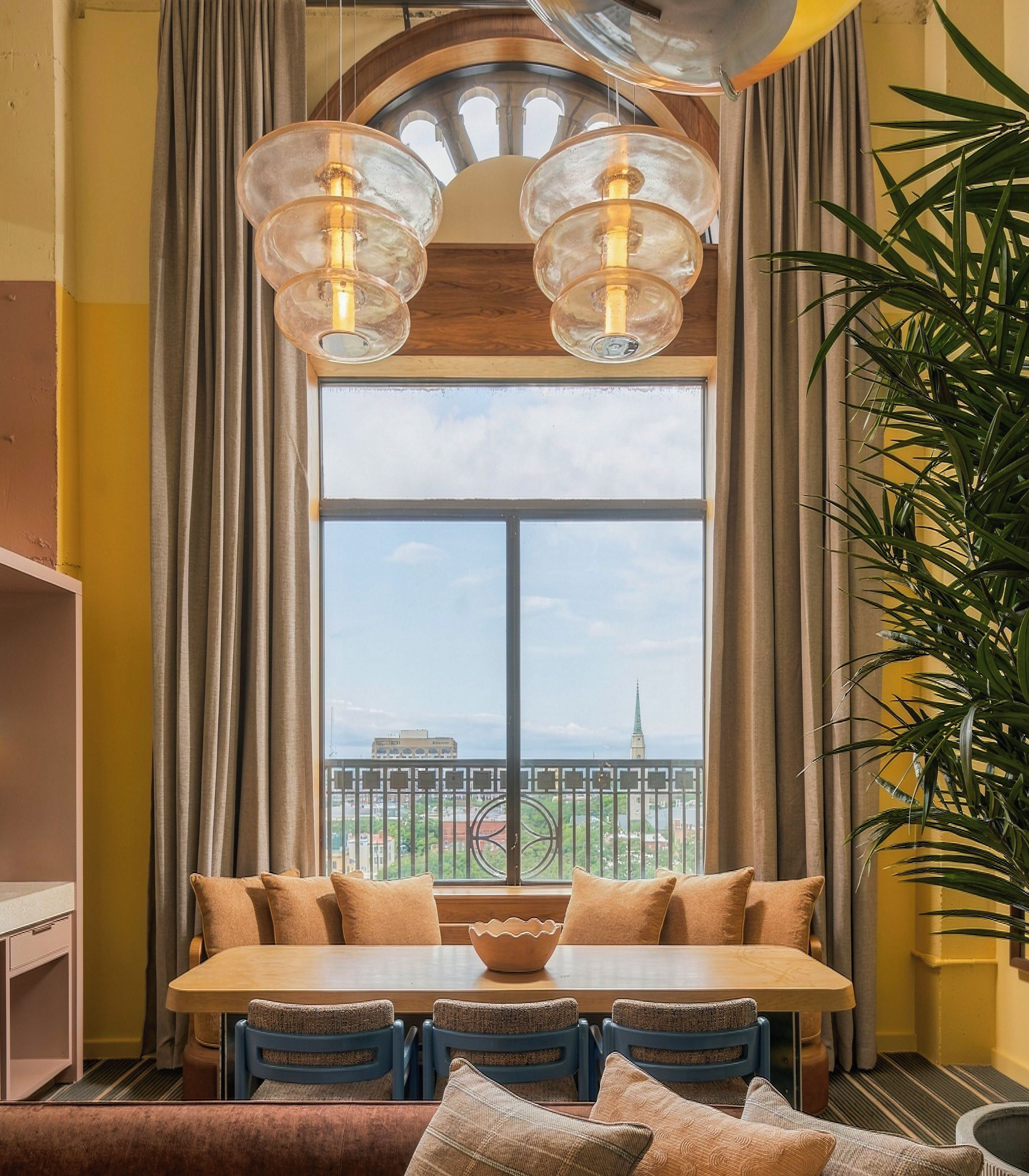 A dining area with a large window, a table with chairs, and a hanging light fixture.
