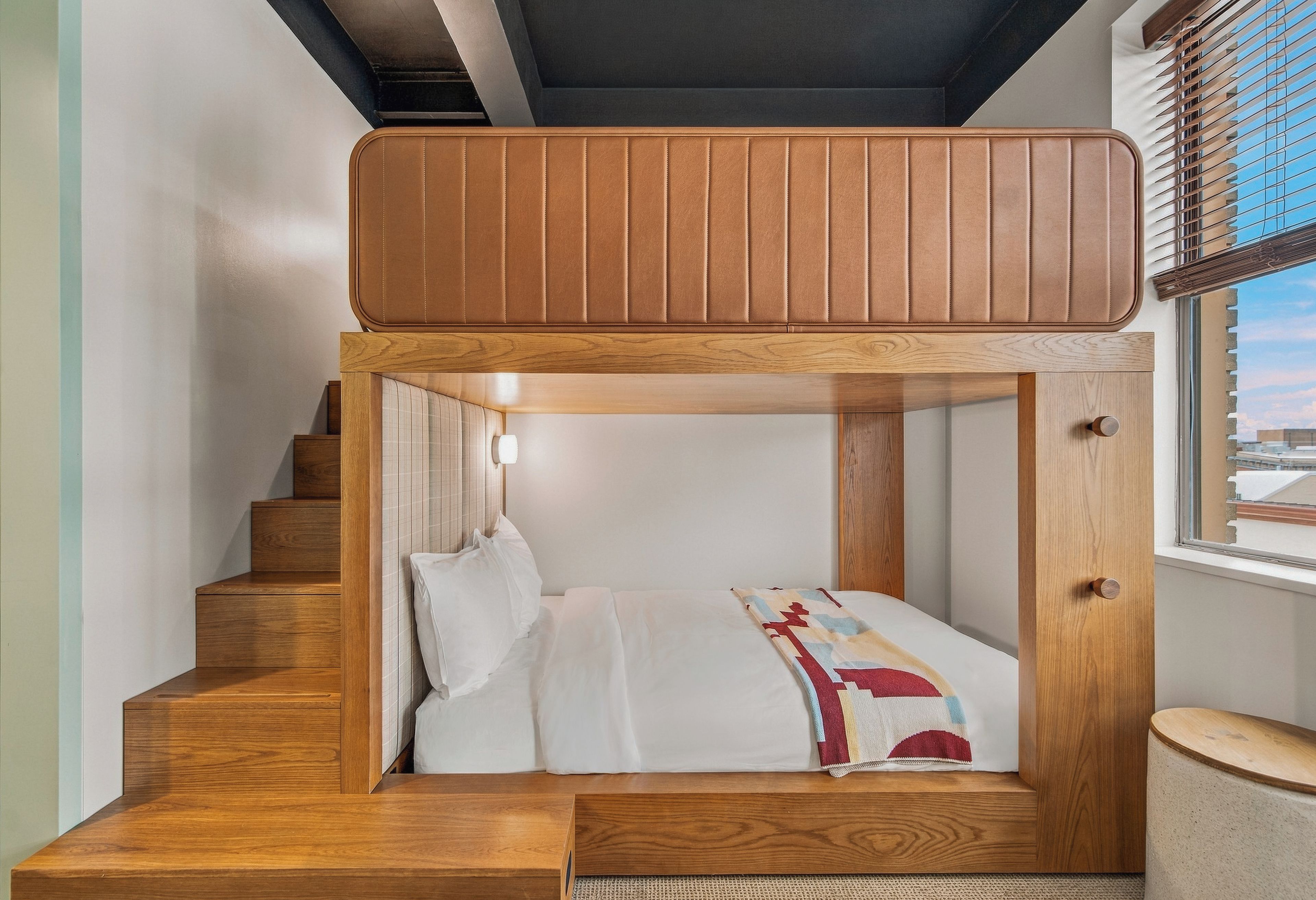 Un lit superposé avec une structure en bois et une fenêtre équipée de stores.