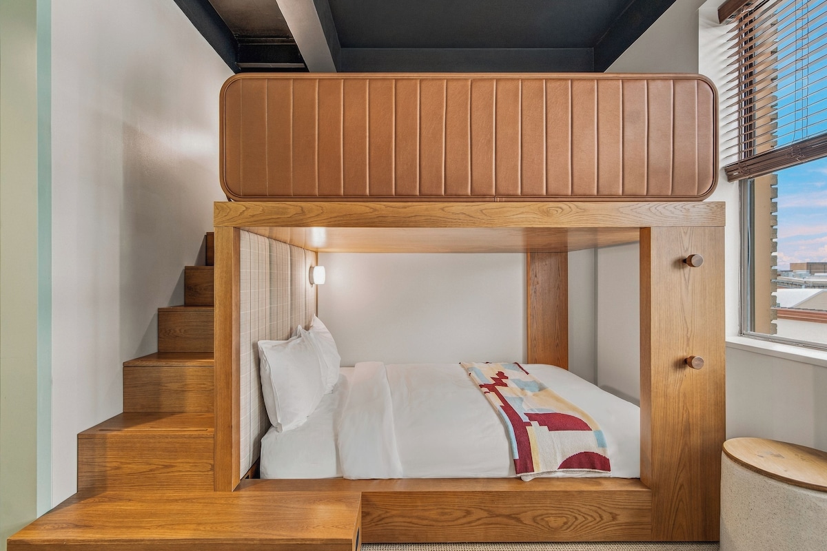 A bunk bed with a wooden frame and a window with blinds.