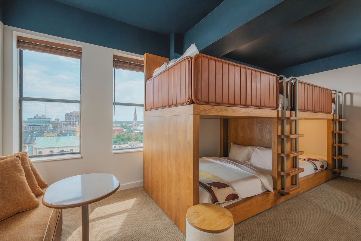 A bunk bed room with a city view, a small table, and a chair.