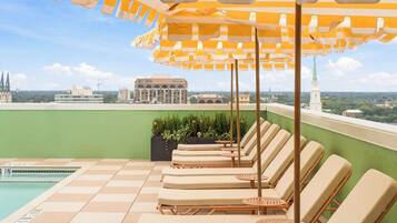 A rooftop pool area with lounge chairs and striped umbrellas, overlooking a cityscape.