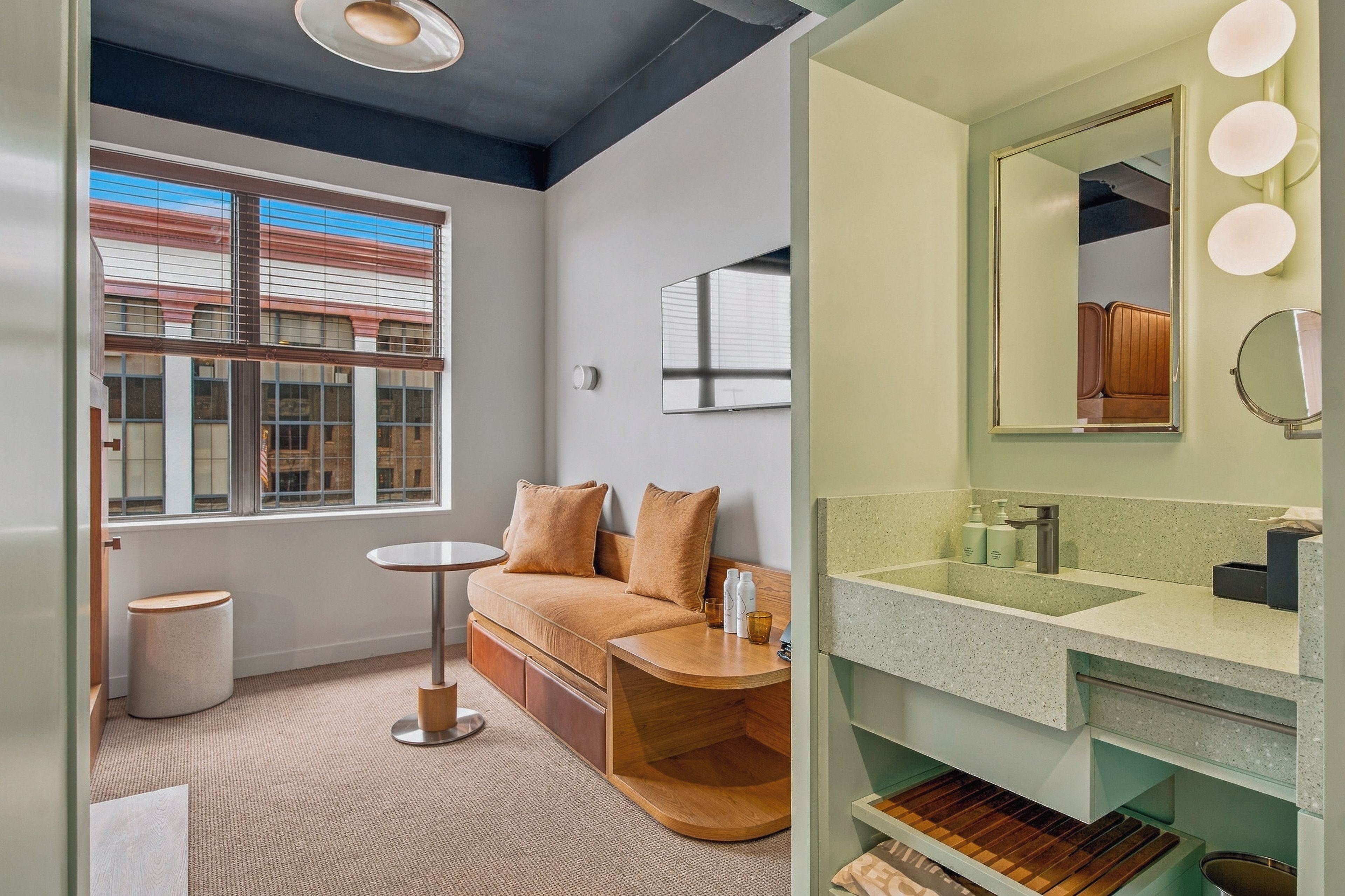 A modern bathroom with a large mirror, vanity, and a window with blinds.