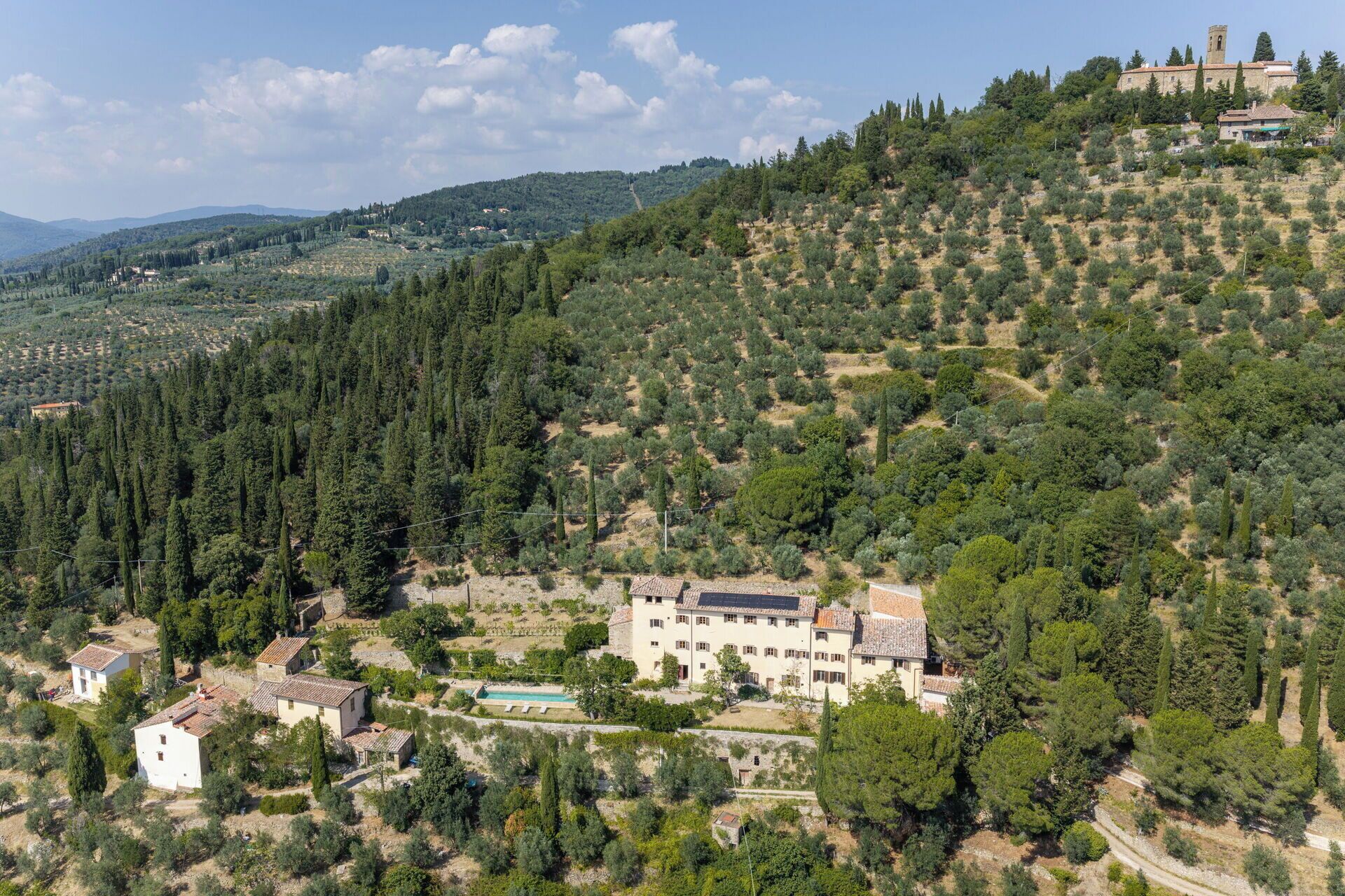 Una villa con piscina, rodeada de olivares y cipreses, situada en una colina.