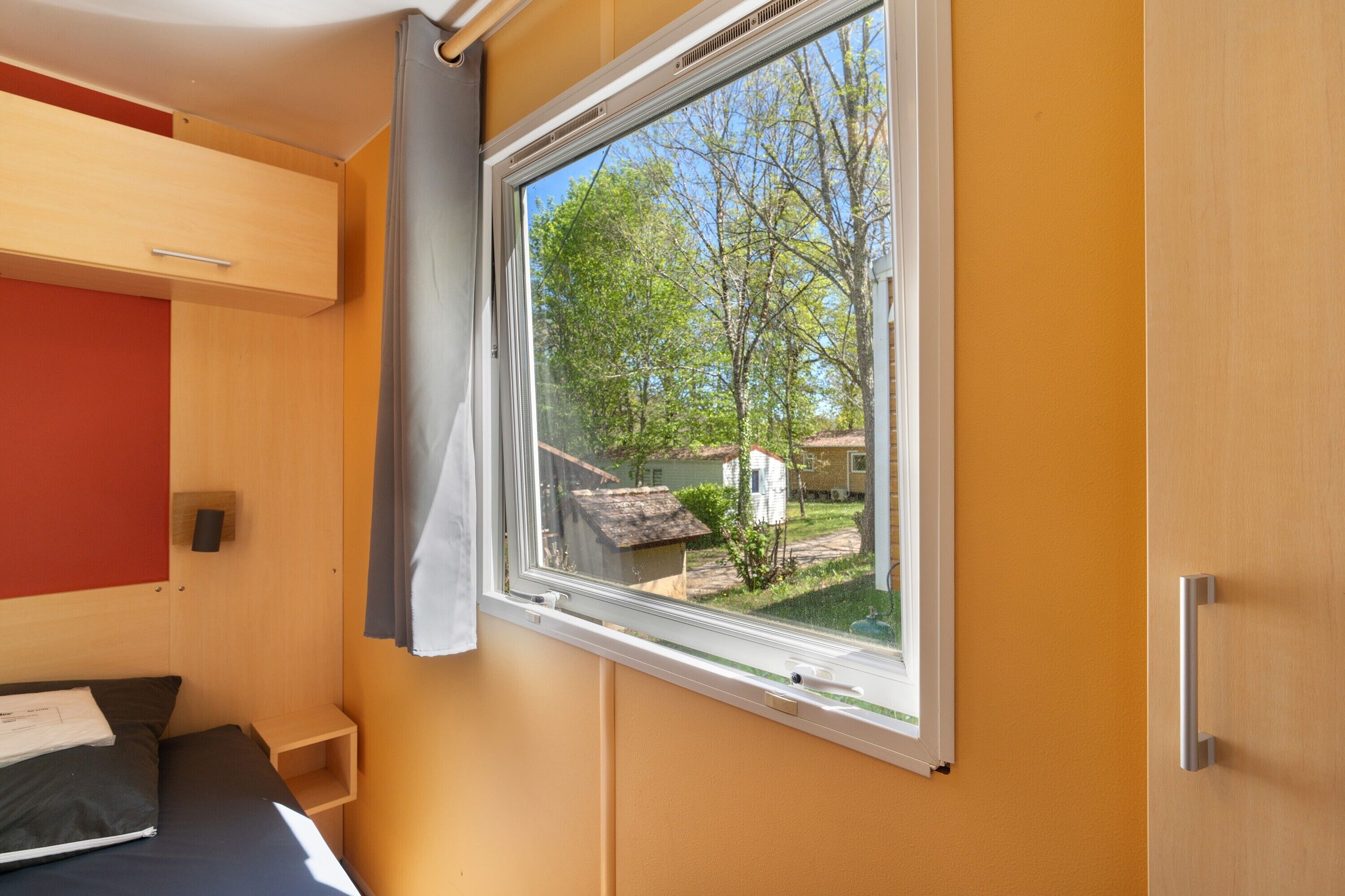 Ein Zimmer mit Fenster, einem Bett, einem kleinen Tisch und einem an der Wand befestigten Regal.