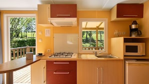 A compact kitchen with a gas stove, sink, microwave, and a window overlooking a deck. - Mobile Home '4 Personnes Climatisé' with Shared Pool, Wi-Fi and Air Conditioning (Saint-Martial-de-Nabirat)