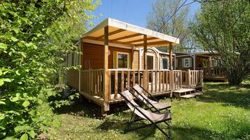 A wooden cabin with a porch, a deck, and a lounge chair.