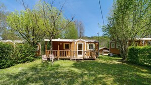 A wooden cabin with a porch, surrounded by greenery and trees. - Mobile Home '4 Personnes Climatisé' with Shared Pool, Wi-Fi and Air Conditioning (Saint-Martial-de-Nabirat)
