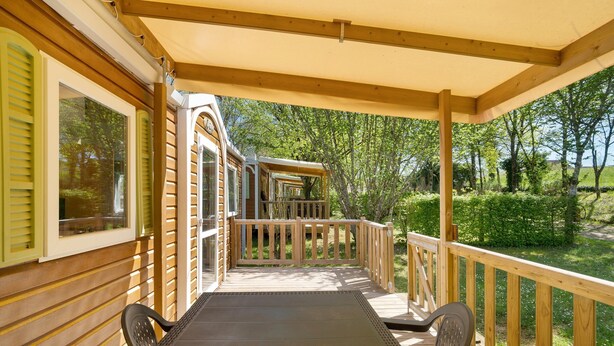A covered outdoor deck with a wooden railing, a table, and chairs. - Mobile Home '4 Personnes Climatisé' with Shared Pool, Wi-Fi and Air Conditioning (Saint-Martial-de-Nabirat)