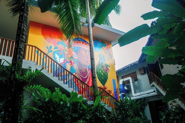 A staircase with a colorful mural, surrounded by lush greenery and a palm tree.