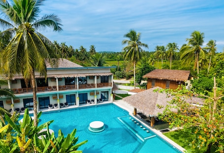 A resort with a swimming pool, thatched-roof structures, and lush greenery.