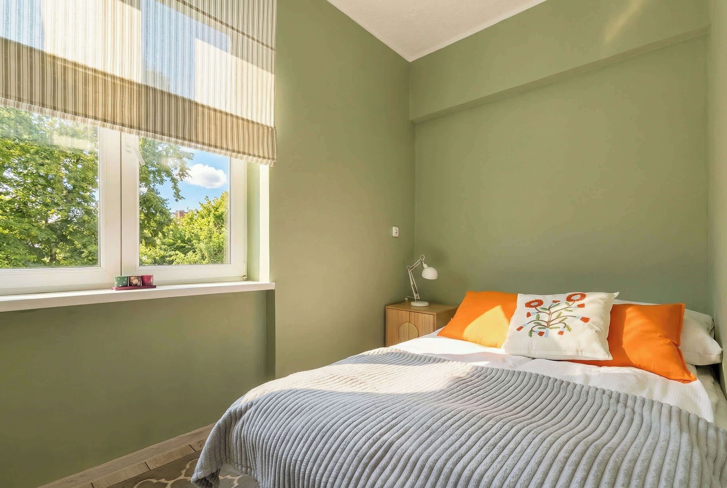 A bedroom with a bed, a nightstand, a lamp, and a window with blinds.