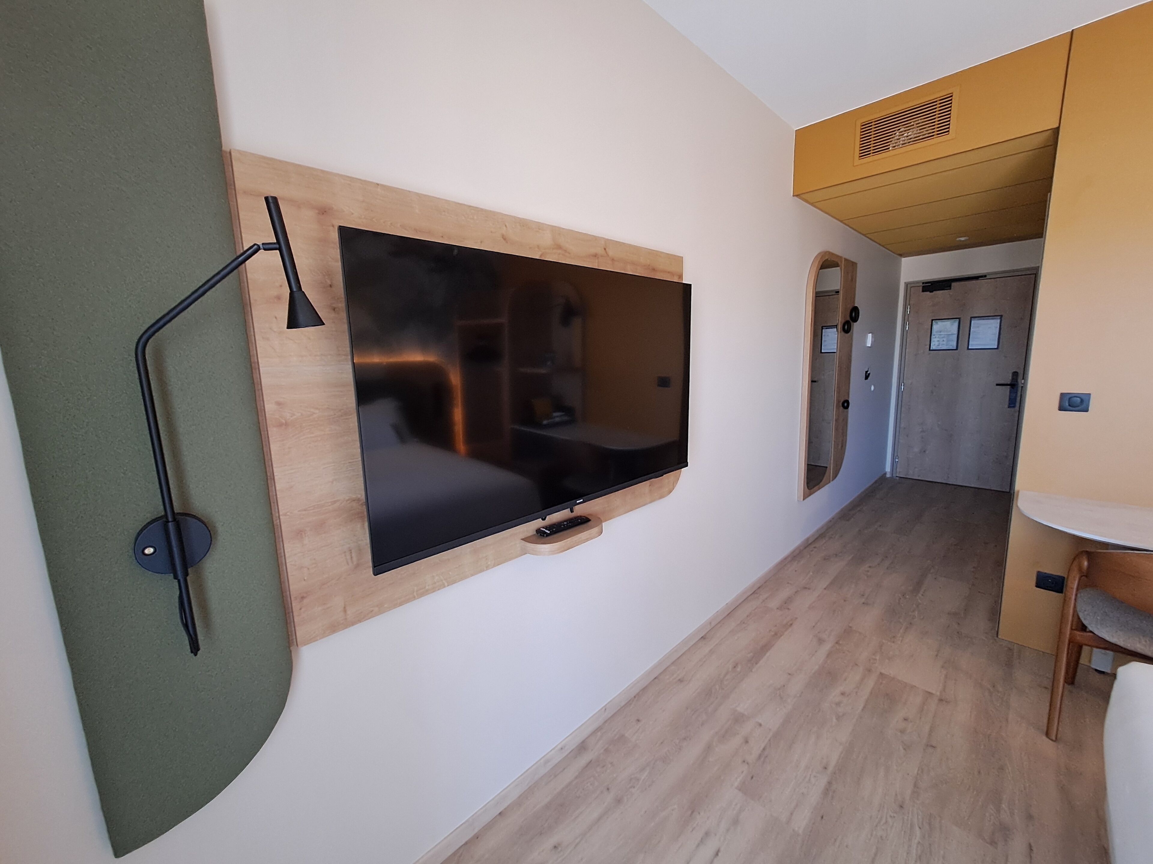 A compact room with a mounted flat-screen TV, a desk, and a chair.