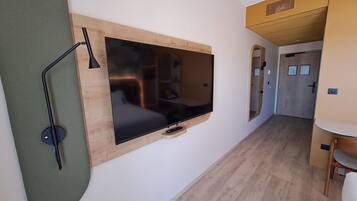 Une chambre de taille modeste, équipée d’un téléviseur à écran plat fixé au mur, d’un bureau et d’une chaise.