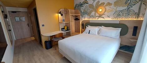 Una habitación de hotel con cama, escritorio, armario y un mural en la pared.