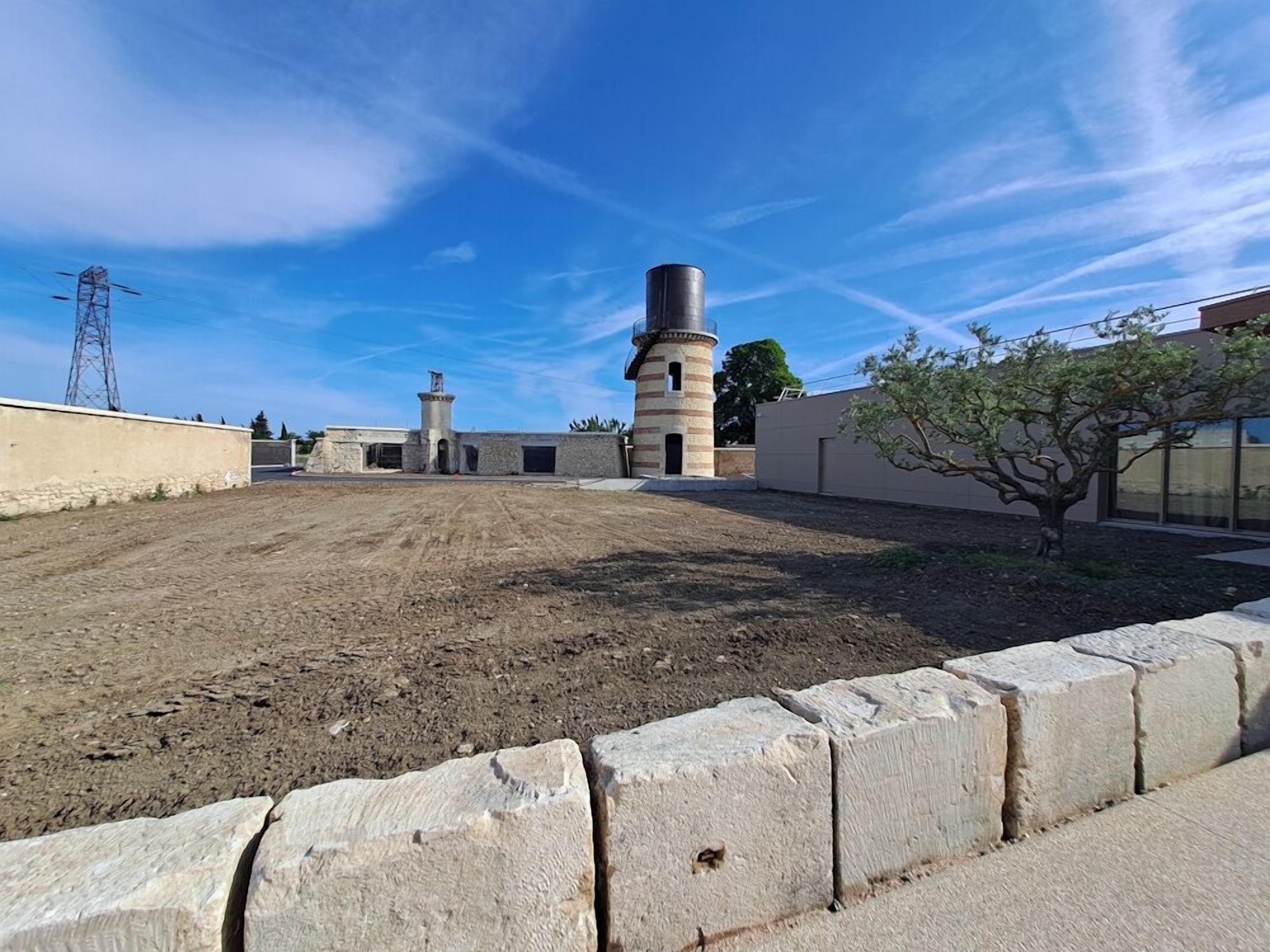 An open area with a stone wall, a tall chimney, and a tree.
