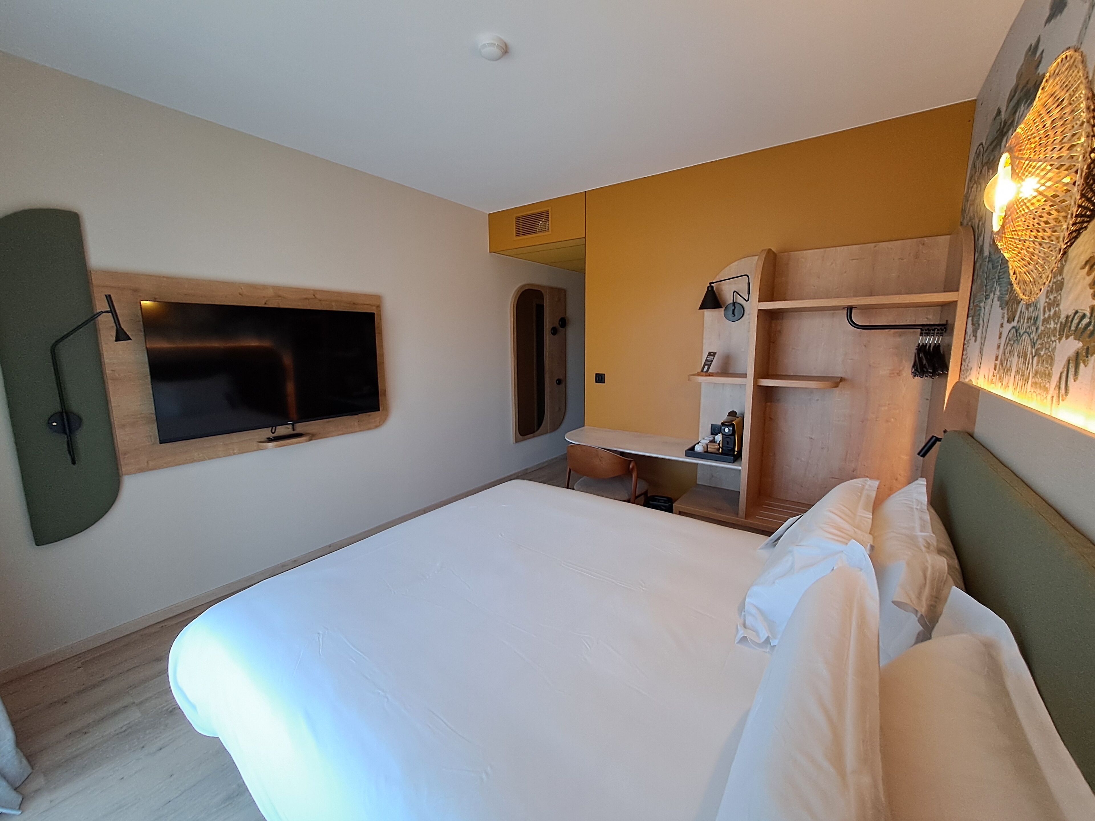 Een hotelkamer met een bed, een bureau, een stoel, een aan de muur bevestigde televisie en een kledingkast.