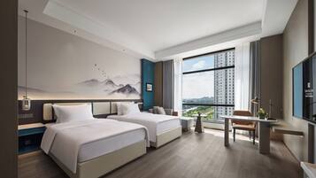Una habitación de hotel moderna con dos camas, un escritorio, una silla, un ventanal con vistas a la ciudad y un televisor montado en la pared.