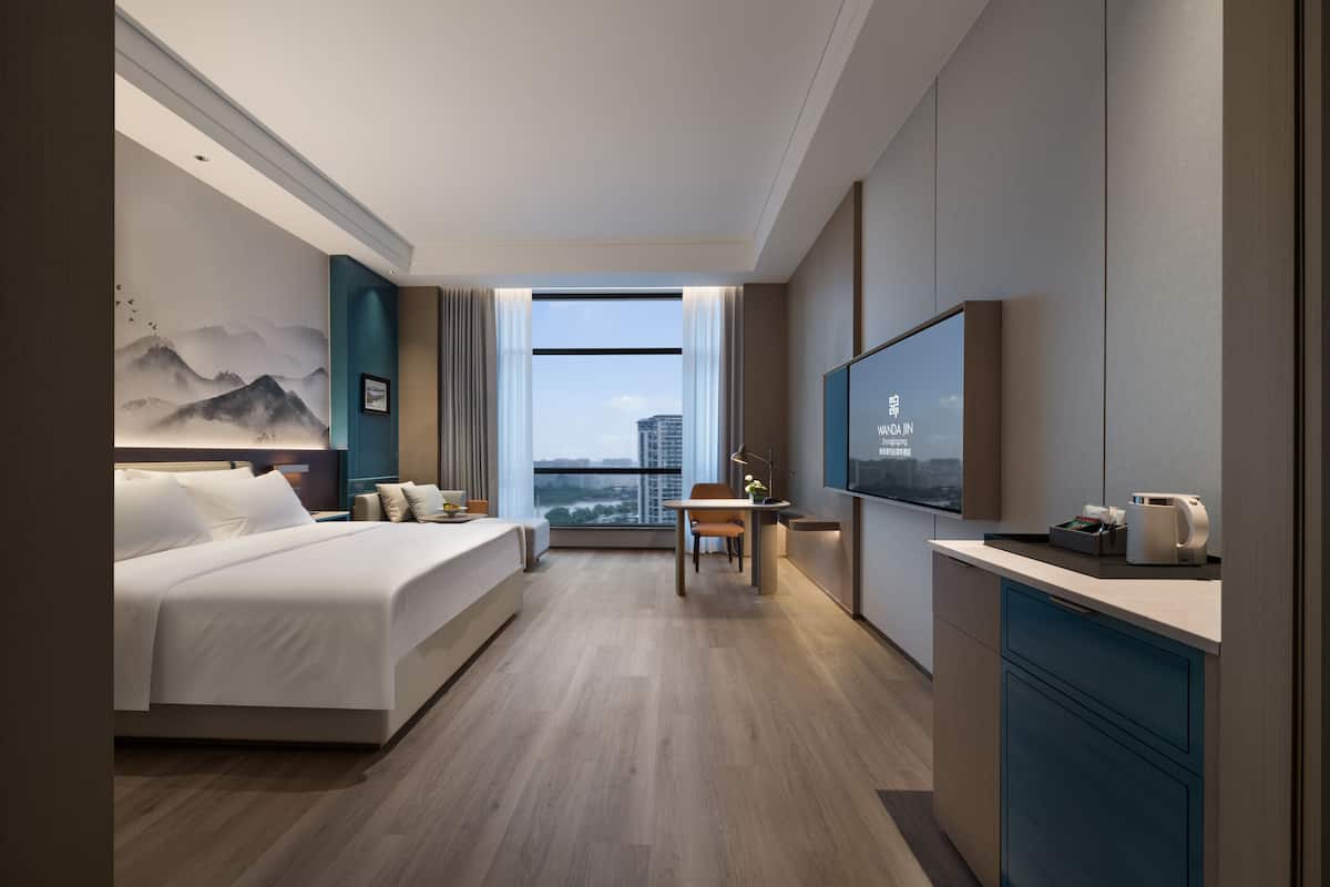 Una habitación de hotel moderna con una cama grande, un escritorio, televisión y vistas a la ciudad.