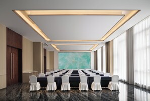 A conference room with a long table, white chairs, and a large screen at the front.