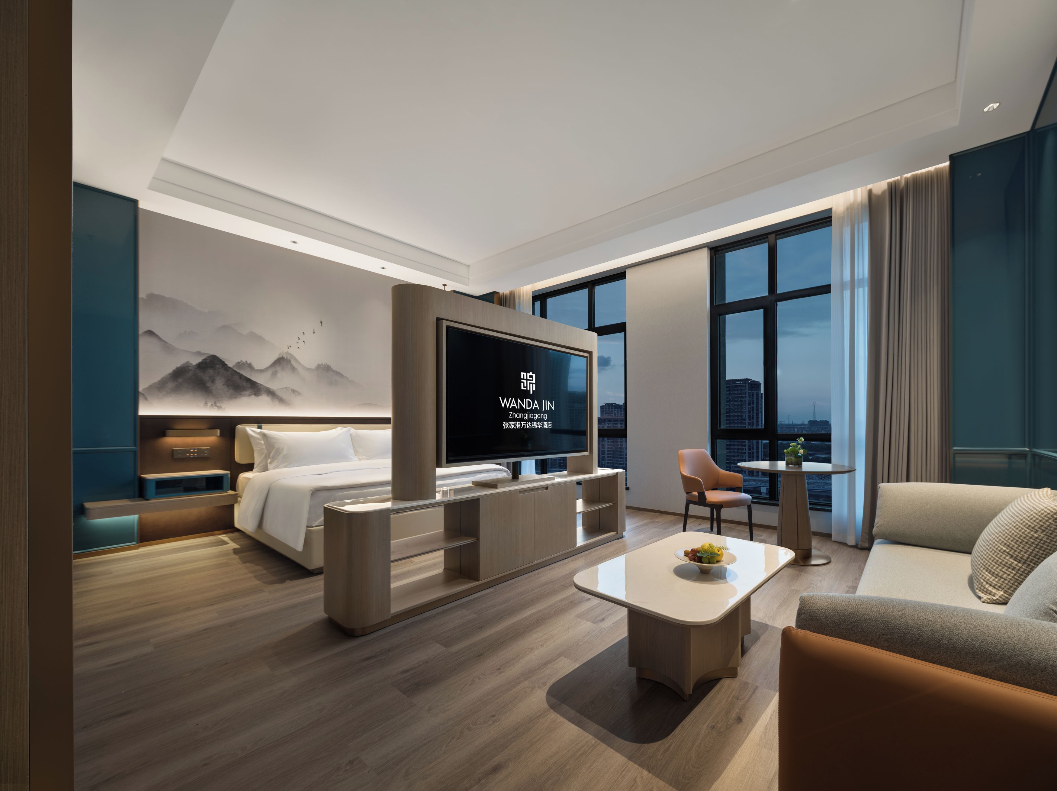 A modern hotel room with a bed, a TV, a sofa, a coffee table, and a city view.