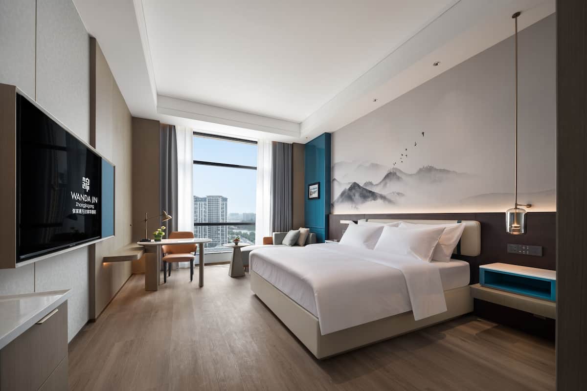 Una habitación de hotel moderna con una cama grande, televisión, escritorio y vistas a la ciudad.