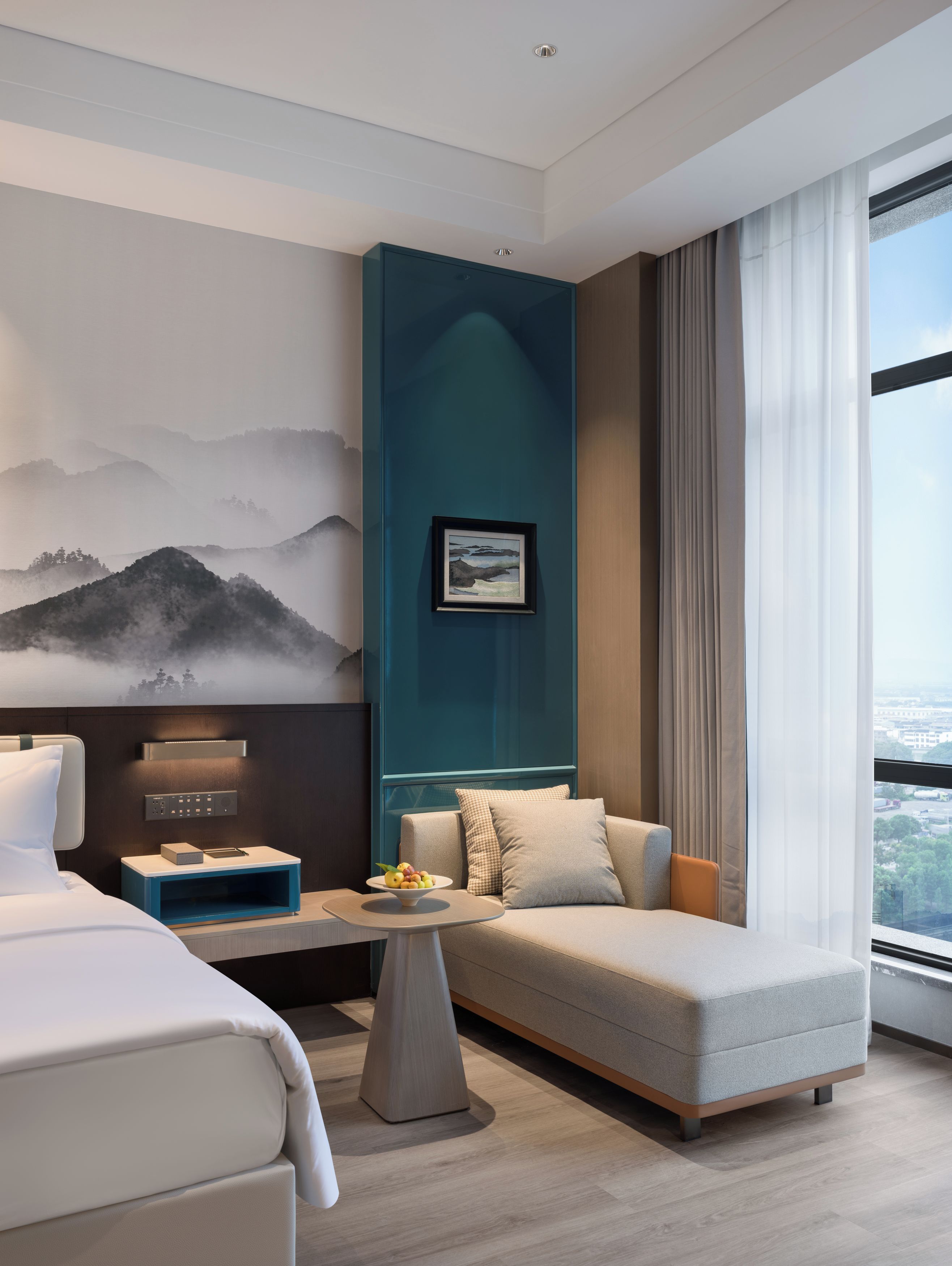 Una habitación de hotel moderna con cama, sofá, mesa de centro y un gran ventanal con vistas.