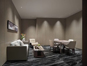 Una habitación de hotel moderna con sofá, sillones, una mesa de comedor y una mesita de centro.