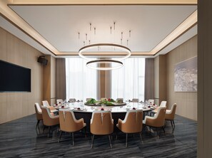 Une salle de conférence équipée d’une table ronde, de chaises, d’un grand écran et d’un lustre moderne.