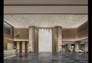 A spacious lobby with a marble reception desk, vertical wooden panels, and a modern ceiling design.