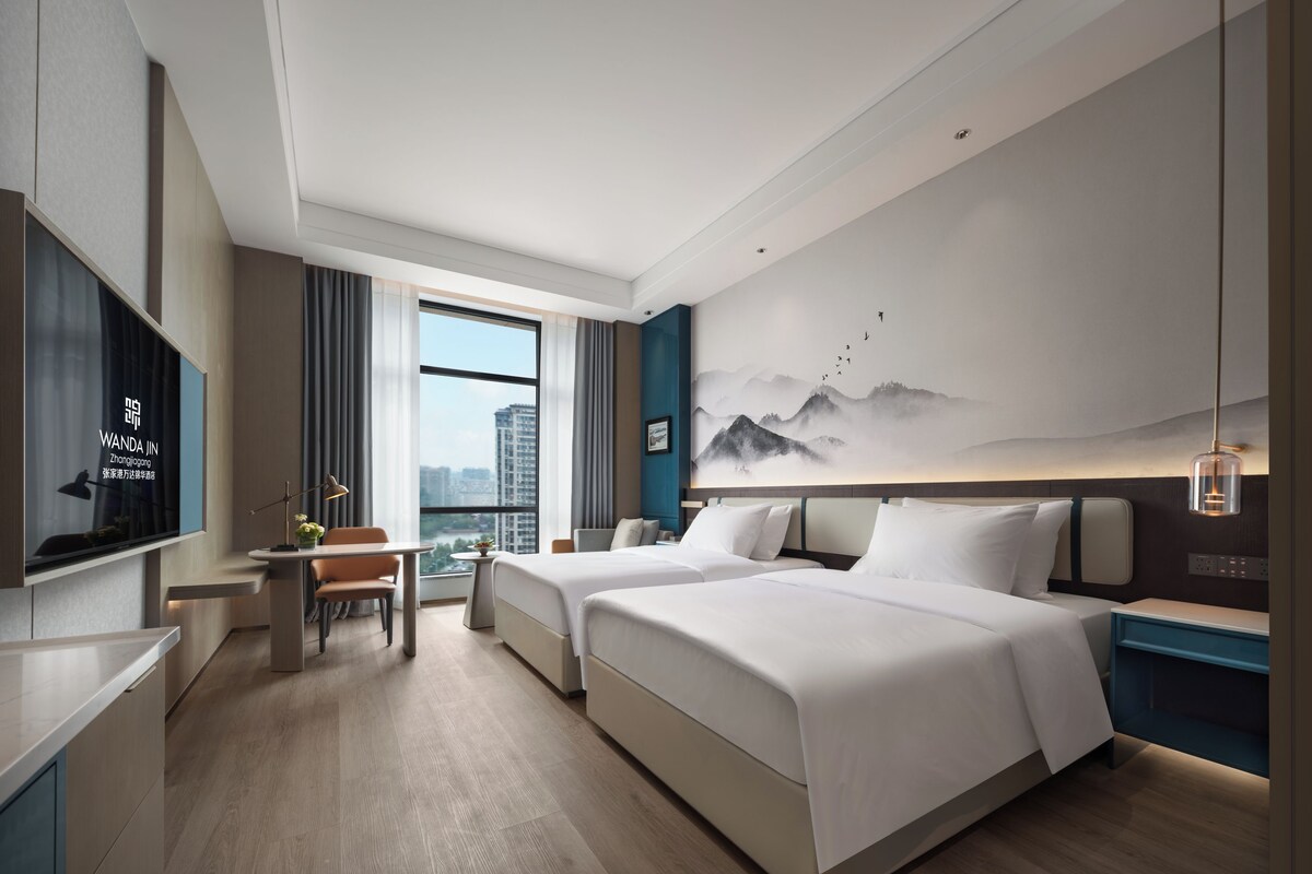 Habitación de hotel con cama, escritorio, silla, televisión y ventana grande.